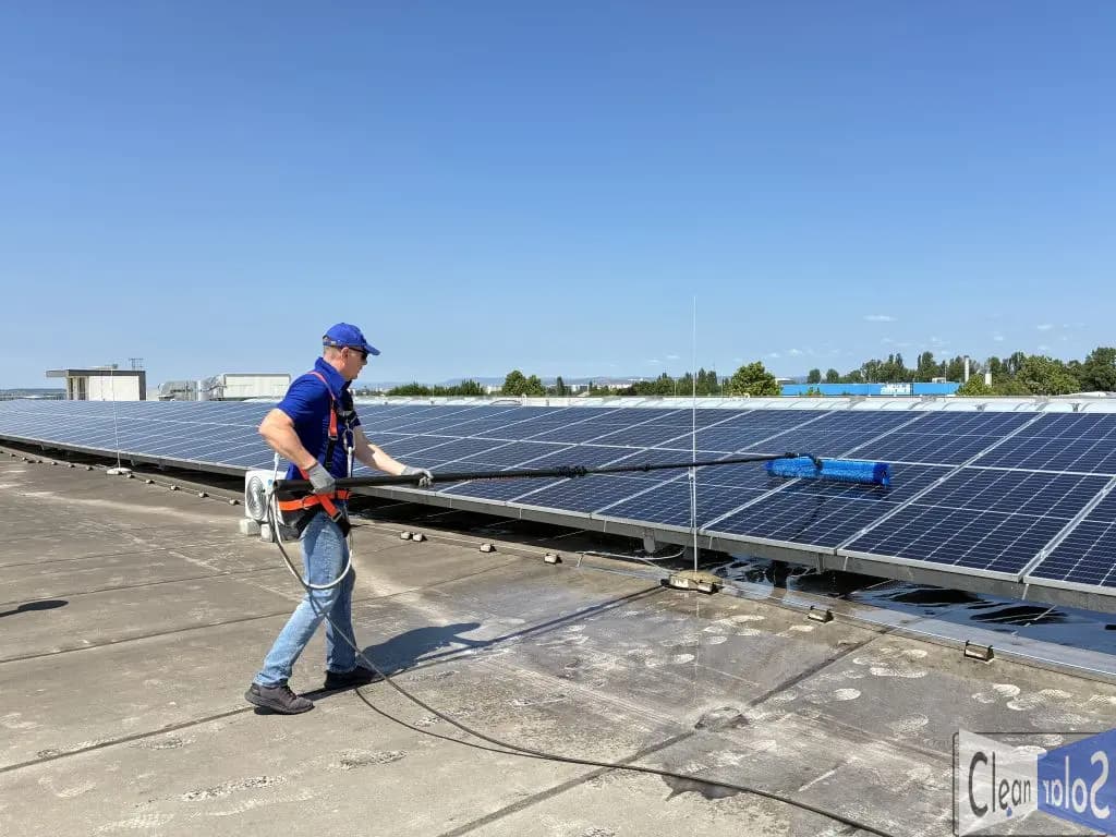 CleanSolar szakember teleszkópos eszközzel, biztonsági hevederben tisztít napelemeket